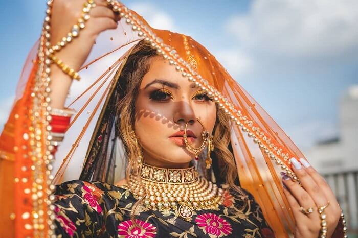 “Full-length bridal portrait of a bride in a white lace gown standing near natural window light, showcasing soft lighting, elegant pose, and detailed wedding dress texture.”